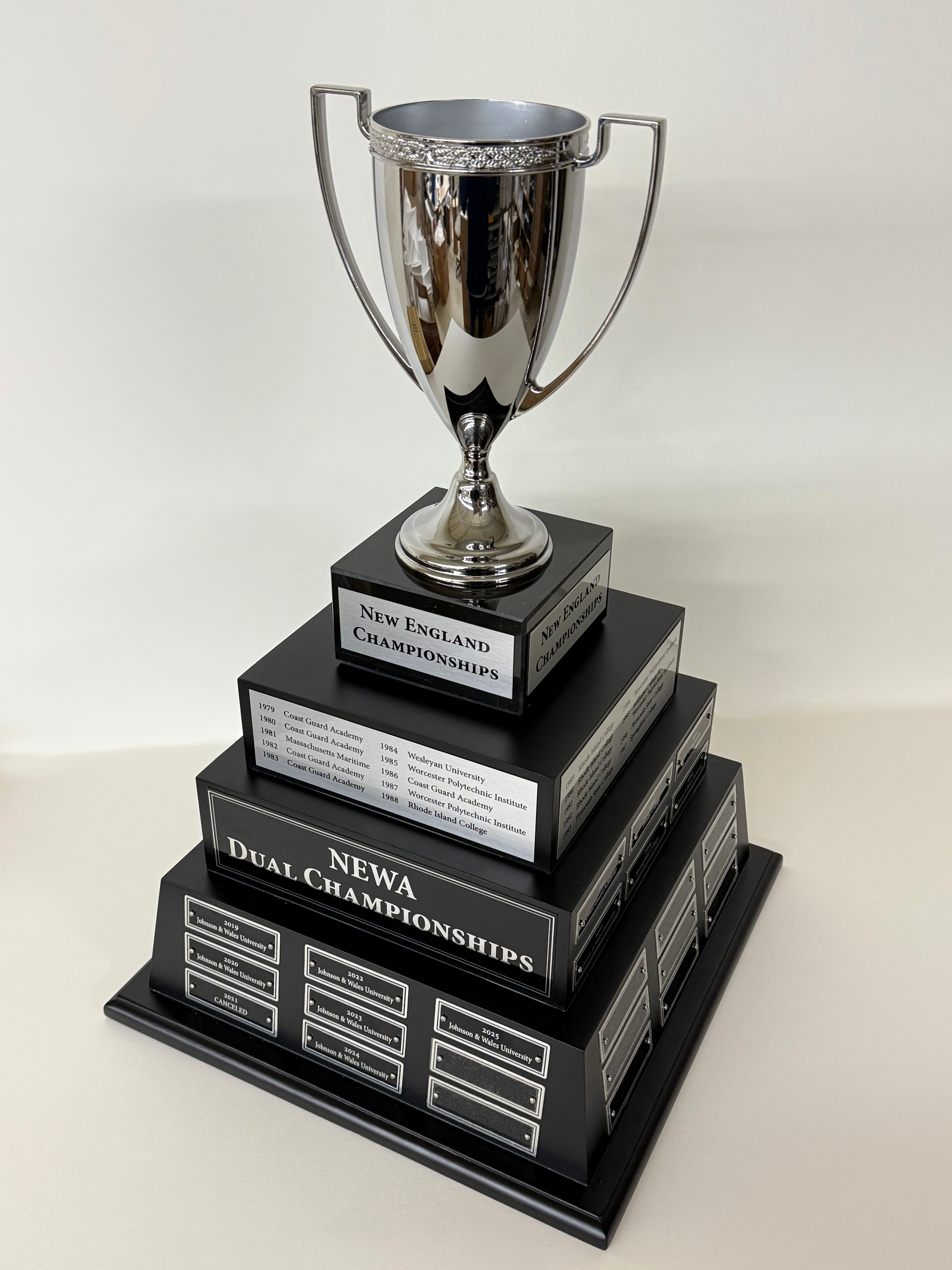 Multi tiered trophy with a metal cup on a black base and engraved text on a white background