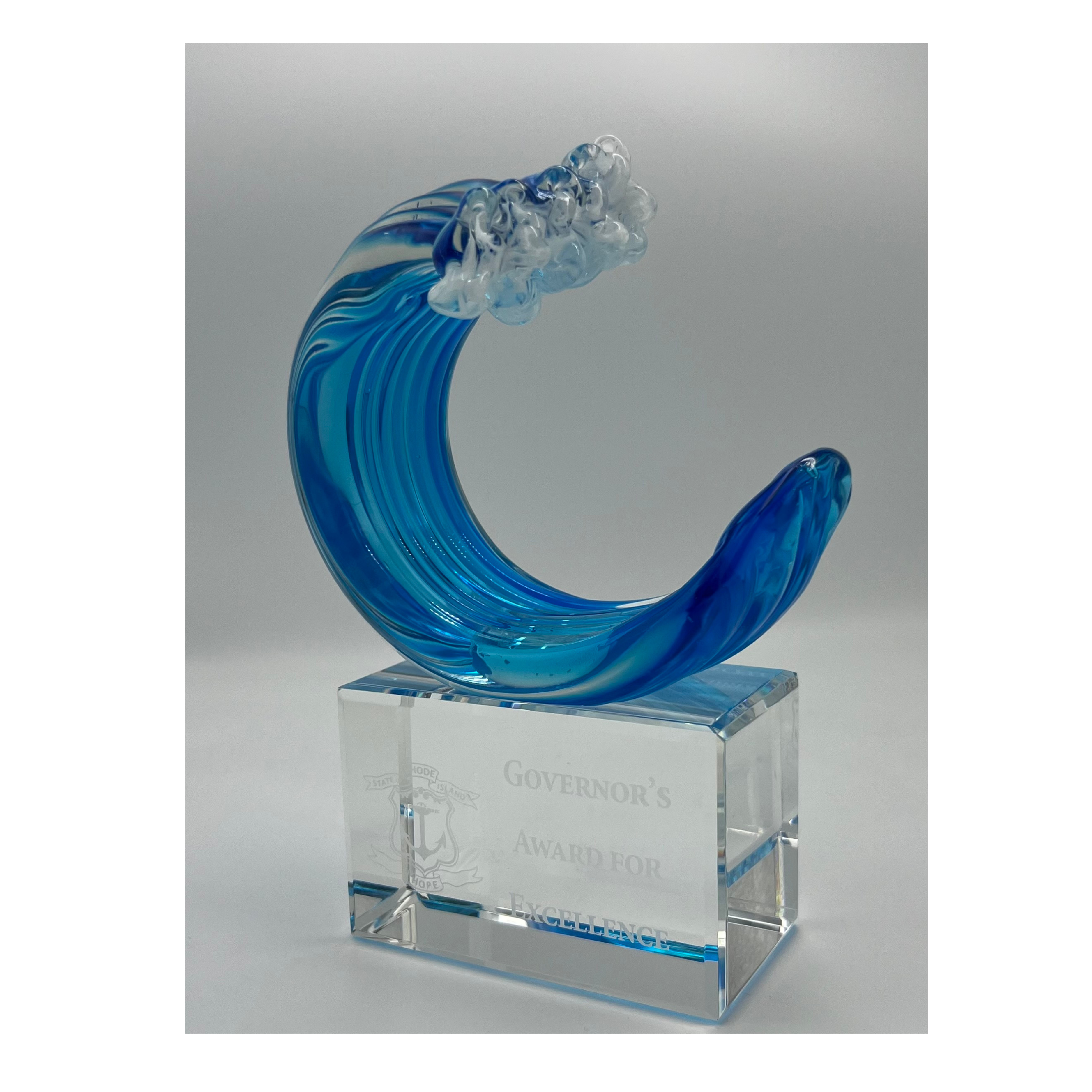 A hand-blown art glass wave, with a clear glass base, predominantly blue in color, with a personalized message etched on the base.