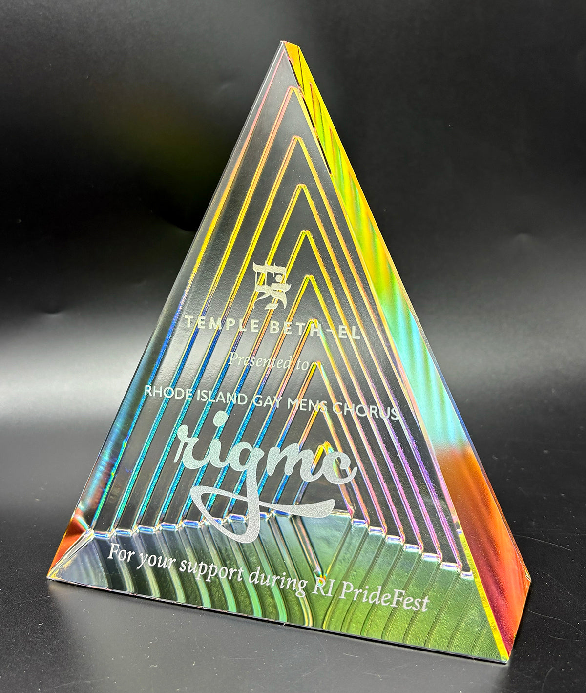Triangular glass award reflecting colors of  the  rainbow and engraved text on a clear background